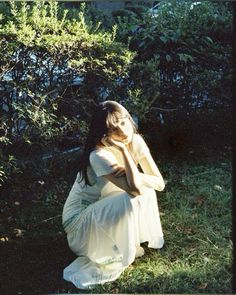 a woman is sitting in the grass with her hands on her face and looking down