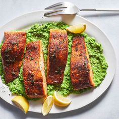 some fish is on a white plate with green sauce and lemon wedges next to it