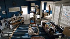 a living room filled with furniture and windows covered in blue blinds, while someone is walking through the window