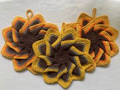 three crocheted flowers are sitting on a white tablecloth with brown, yellow and orange colors