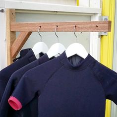 three wetsuits are hanging on hooks in front of a yellow door and window