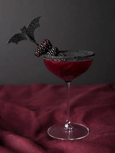 a red drink in a martini glass with a black bat garnish on top