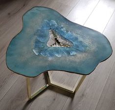 a glass table with a blue flower design on the top and gold legs, sitting on a wood floor