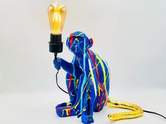 a blue monkey holding a light bulb on top of it's head and sitting next to a banana