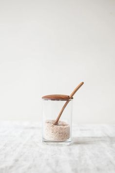 a wooden spoon sticking out of a glass container filled with sand and sea salt on a white tablecloth