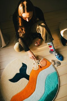 a woman sitting on the floor working on a rug