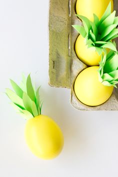 three yellow eggs sitting next to each other on top of a white surface with green leaves