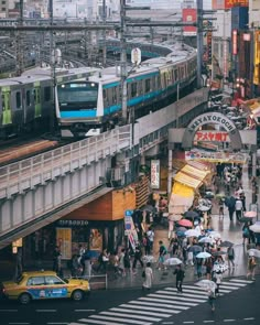 many people are walking on the street with umbrellas in front of a train station