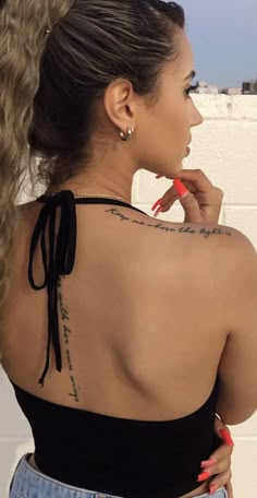 a woman with her back to the camera and tattoos on her upper half, looking off into the distance