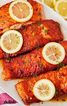 baked fish with lemons and herbs on a white plate next to sliced lemons