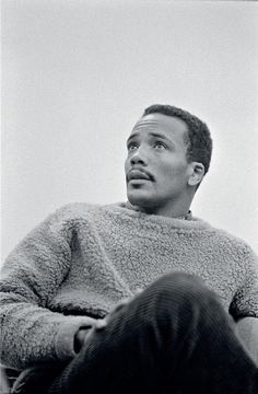 a black and white photo of a man in a fuzzy sweater looking up at the sky