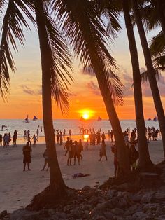 many people are on the beach at sunset with palm trees and boats in the water