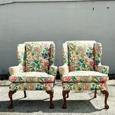 two chairs sitting next to each other in front of a gray wall with flowers on it