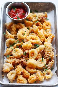 a tray filled with fried food next to a bowl of ketchup and sauce