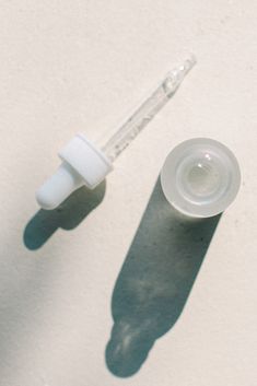 an empty bottle with a dropper next to it on a white surface and the shadow of a person's hand