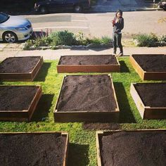 a woman standing in front of a row of raised garden beds filled with dirt and grass