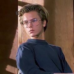 a young man wearing glasses standing next to a wooden wall