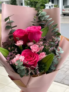 a bouquet of pink roses and greenery in a wrapper on the street corner