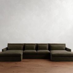 a large green couch sitting on top of a wooden floor next to a white wall