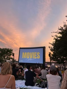 people are sitting in the grass watching movies on a big screen at sunset or dawn