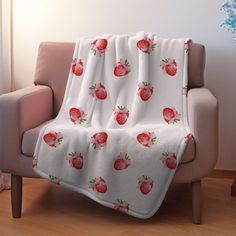 a white blanket with strawberries on it sitting on a chair in front of a window