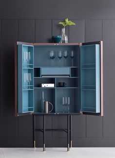 an open cabinet with wine glasses and cups in it on a white floor next to a gray wall