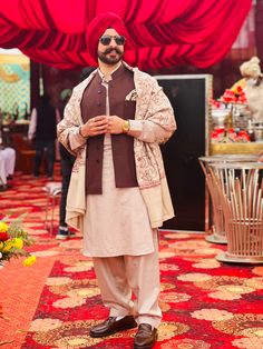 a man in a turban standing on a carpet with red curtains behind him