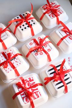 six square cakes with red ribbons tied around them on a white tablecloth covered tray