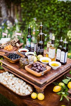 an assortment of olives and other foods on a wooden tray with bottles of wine