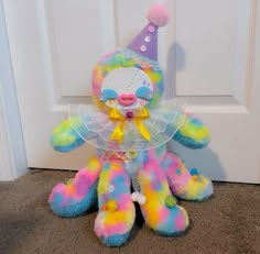 a rainbow colored stuffed animal sitting in front of a door