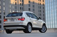 the rear end of a white bmw suv parked in front of tall buildings on a city street