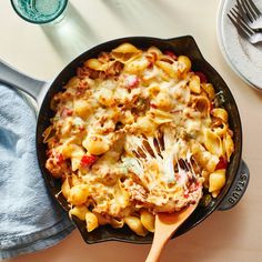 a skillet filled with pasta and sauce on top of a table next to silverware