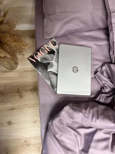 a laptop computer sitting on top of a bed next to a vase with dried flowers