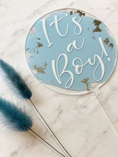 it's a boy sign and two blue feathers on a marble counter top with the words it's a boy written in white