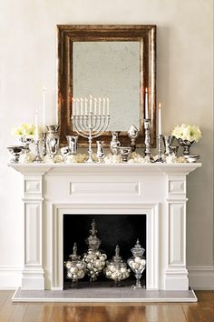 a mantel with candles and flowers on it in front of a mirror above the fireplace