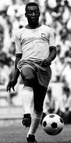 a black and white photo of a man kicking a soccer ball in front of an audience