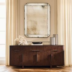 a large mirror hanging on the wall above a wooden cabinet with vases and books