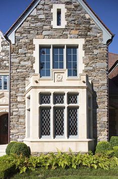 a stone house with large windows and bushes in front