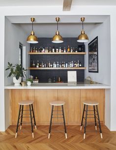 three stools sit in front of a bar with bottles on the shelves and lights above it