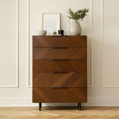 a wooden chest of drawers sitting on top of a hard wood floor next to a white wall