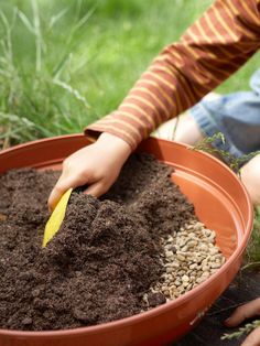 a child scooping dirt into a bowl filled with grass and sunflower seeds on the ground