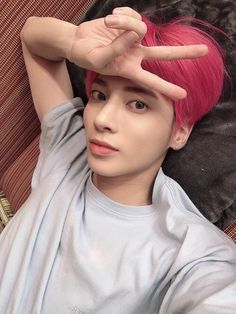 a young man with pink hair laying on top of a couch holding his hands up