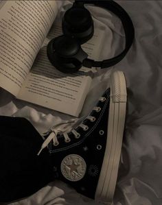 an open book, headphones and converse sneakers on a bed