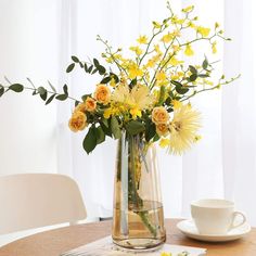 a vase with yellow flowers on a table next to a coffee cup and saucer