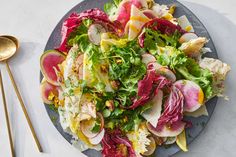 a salad with radishes and lettuce on a plate next to two gold spoons