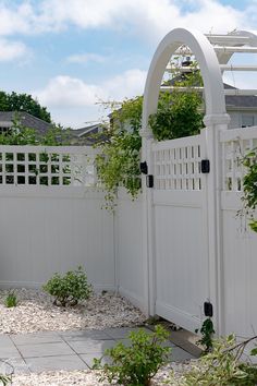 a white fence with an arch in the middle and some plants growing on it's sides