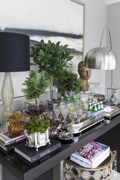 a black table topped with lots of books and vases next to a painting on the wall