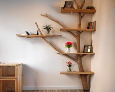 a tree shaped shelf in the corner of a room with flowers and books on it