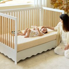 a woman sitting next to a baby in a white crib