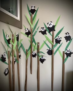 some pandas are sitting on bamboo sticks and hanging from the wall in front of them